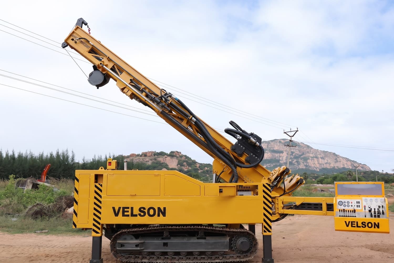 Velson V9 XL crawler drill, side view with the mast at an incline, hydraulic hose runs and winch visible along the feed beam