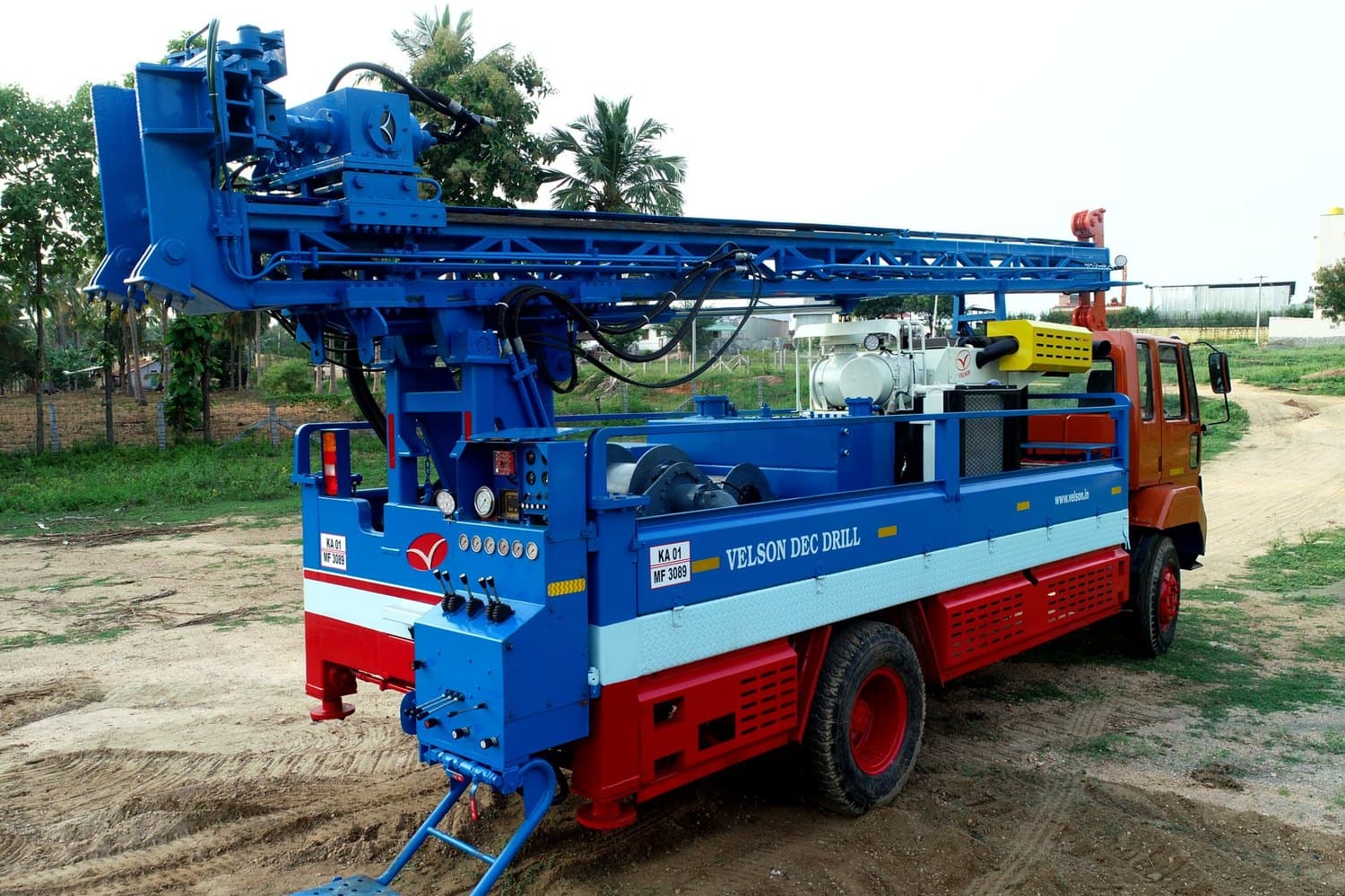 Velson DEC Drill truck-mounted core drill, blue mast folded back along the deck and rear jacks down on a rural site